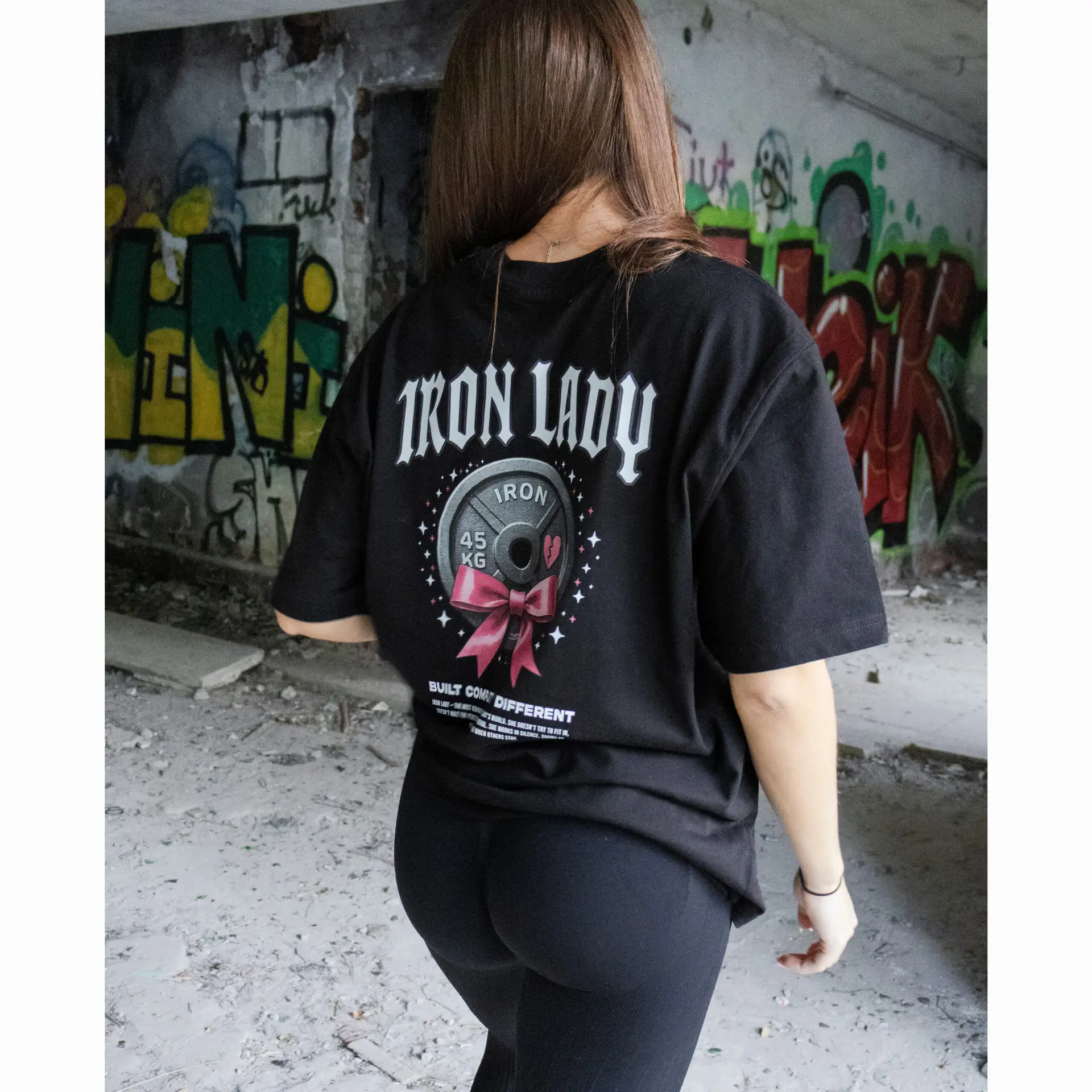 damska koszulka oversize Iron Lady z dużą grafiką talerza i kokardy, ujęcie tyłu na modelce w graffiti scenerii